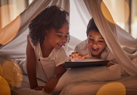 Children, tablet and night streaming online for movies, cartoon or educational games before bedtime in a blanket fort with a fun app. Excited boy and girl kid sharing, reading and internet addictionの写真素材