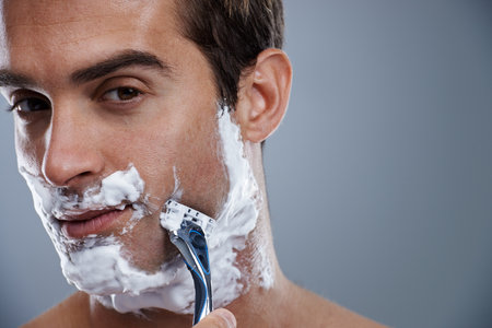 GEtting the closest shave ever. Head and shoulders studio shot of a young man shaving.の写真素材