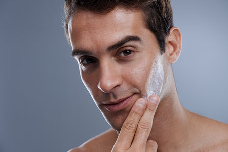 Even men like to be soft....Studio shot of a handsome young man applying cream to his face.の写真素材