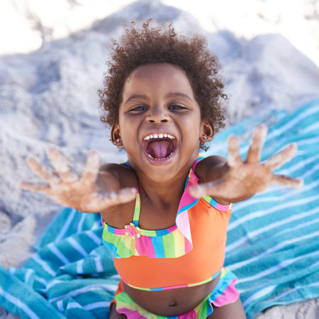 No school for me - Im on holiday. A happy young african girl having fun on the beach and looking at the camera.の写真素材