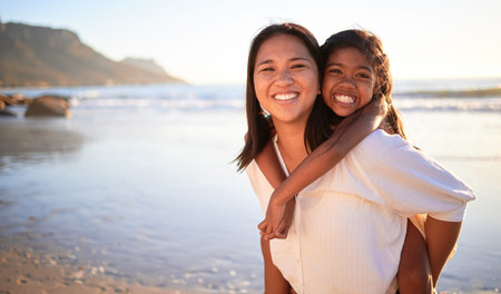 Happy mother and girl have fun together at the beach in the sun on summer vacation. Carefree woman carrying excited child while bonding outdoor. Single mom enjoy quality time with kid at the oceanの写真素材