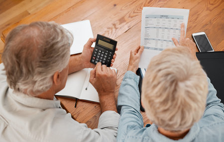 Budget, finance and senior couple with calculator planning financial investments, mortgage and tax papers. Elderly woman counting bills, debt and pension fund on bank statement with partner at homeの写真素材