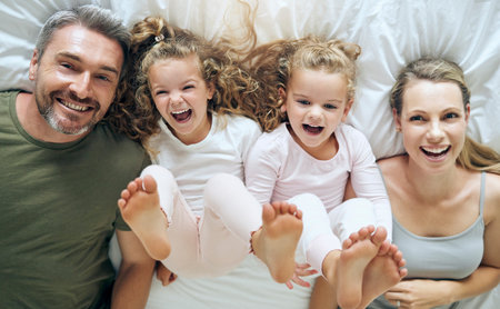 Top view, happy and family with twins in bed smiling together with parents in the morning at home on the weekend. Kids, smile and playful girls enjoy quality time with mother and father on Sundayの写真素材