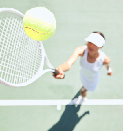 Tennis woman on tennis court with a tennis ball in the air. Closeup of a young female athlete hitting the ball with a tennis racket to serve during a game or match. Training, fun and sports in actionの写真素材