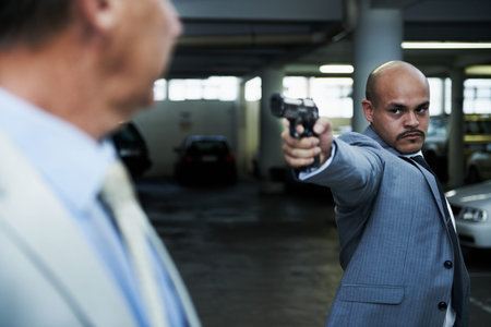 Come with me and come quietly. An angry gangster pointing his handgun at a shocked businessman in a...