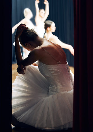 Dancer thinking backstage at ballet concert or recital while group on theater stage. Girl ballerina waiting on floor of auditorium, anxiety and nerves, for performance in front of audience or crowdの写真素材