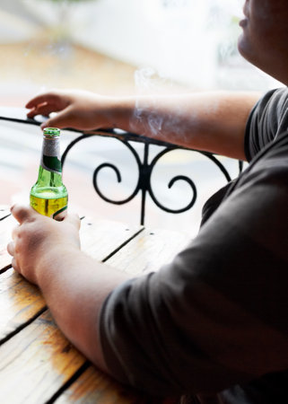 Indulging in lifes little pleasures. A cropped image of a young man smoking while sitting with a beer in front of him.の写真素材