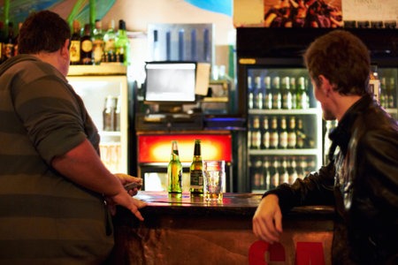 Wheres the service in this place. Two young men standing at a bar counter.