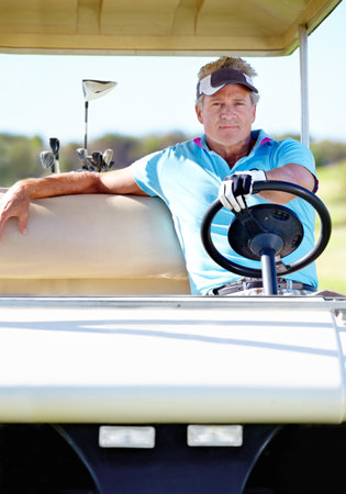 This really is relaxation exercise. A mature man sitting behind the wheel of a golf cart and looking at the camera.の写真素材