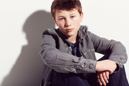 Keeping things casual. Young adolescent boy sitting against a white background.