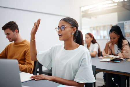 Education through questions by students at university with diversity during lecture. Young woman in classroom, asking with hand up while classmate listen on. Motivation through discussion.の写真素材