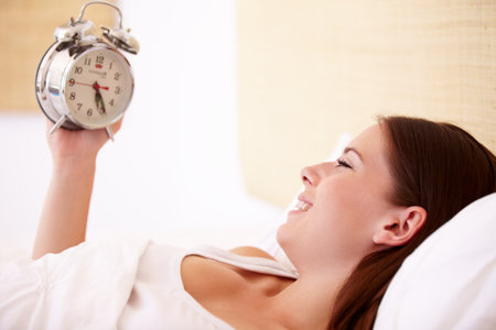 Oh dear, Ive slept all day. A gorgeous young woman smiling while looking at her alarm clock.の写真素材