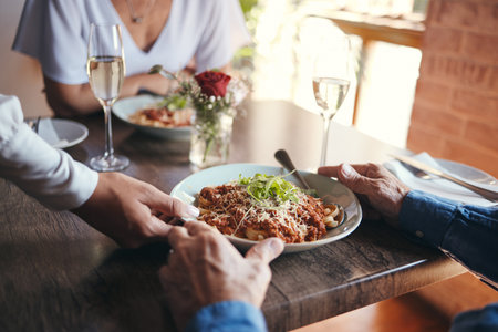 Food service, wine and couple at table with hospitality from waiter at restaurant for lunch. Cafe worker with plate of pasta for man and woman on date for anniversary or marriage at fine dining cafeの写真素材