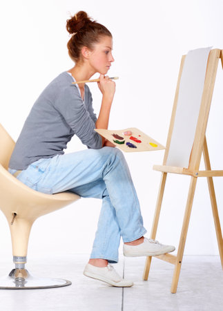 Ideas are not coming fast today. Studio shot of a young woman sitting on a chair looking at a blank canvas.の写真素材