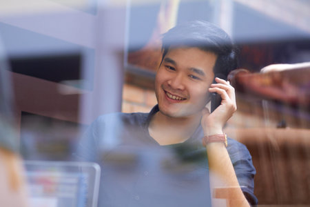 Taking a call from a loved one. Smiling Asian man using a mobile phone indoors.
