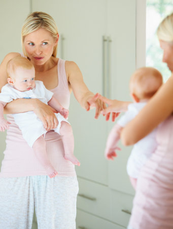 Motherhood in reflection. A lovely mother pointing at the reflection in the mirror while holding her...
