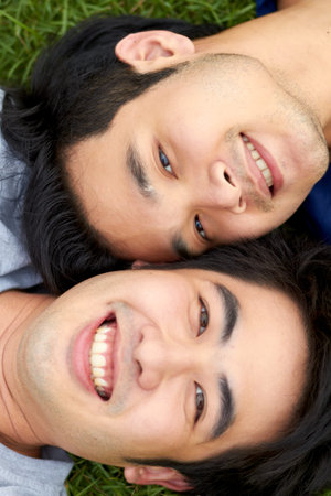 Sharing a special bond. Cute young gay Asian couple smiling together and looking up at the camera.