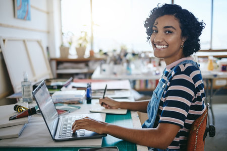Creative black woman, smile and laptop working in art studio, workshop or design startup with...