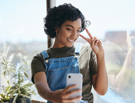Student woman and smartphone selfie with peace hand for social media leisure picture with smile. Young, happy and indian hipster girl enjoying break with phone photograph for internet app.の写真素材