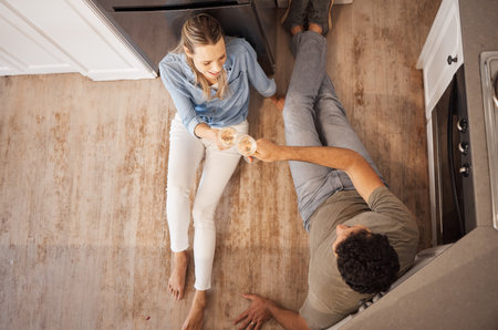 Champagne, cheers and happy couple on the kitchen floor celebrating their new home renovations. Top view of happiness, sparkling wine and toast to the family house of man and woman relaxing together.の写真素材