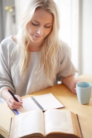 Making notes. A pretty young woman making notes from a book while enjoying a cup of coffee.