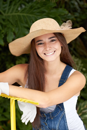 Keeping her garden tidy. Portrait of an attractive young woman leaning on a rake.の写真素材