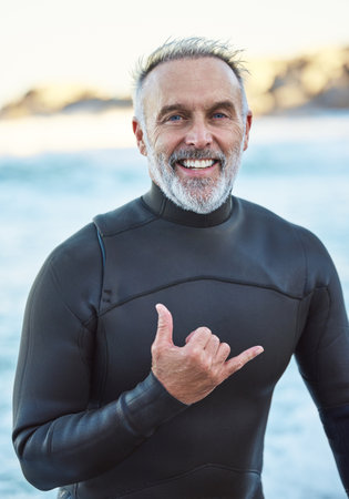 Elderly, surfer and beach with hand sign for portrait with smile in summer by ocean for wellness, fitness and health. Senior, man and surf by sea in retirement on vacation, holiday or travel to Miamiの写真素材