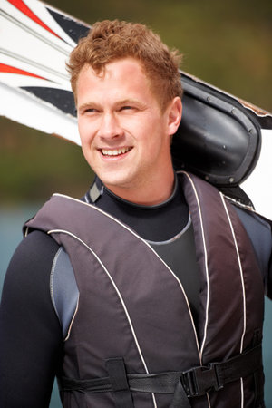 Ready to get out on the waves. Smiling water-skier holding his skis alongside the lake.の写真素材