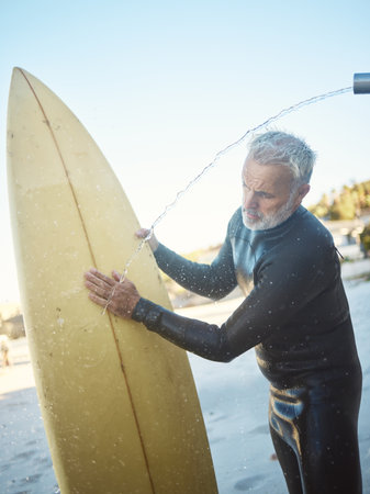 Old man, beach and surfer cleaning surfboard, surfing in Mexico on summer holiday or vacation. Washing, shower and elderly retired male remove sand on board after surf or training exercise in ocean.の写真素材