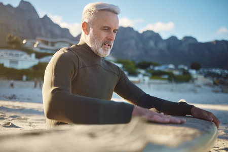 Surf, sand and sports with a man on the beach for surfing, training or exercise on a summer day. Fitness, workout and travel with a mature surfer cleaning a surfboard while on retirement vacationの写真素材