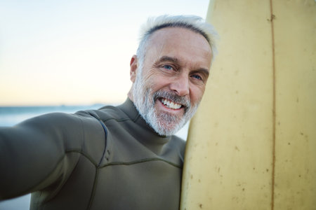 Beach, selfie and happy senior surfer in retirement with surfboard training by the ocean. Happiness, freedom and portrait of an elderly man with smile taking picture while surfing on tropical holidayの写真素材
