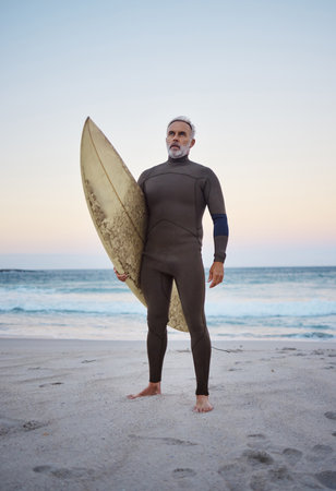 Senior man on beach, summer surfing vacation and holiday travel fitness adventure on Australia shore. Sunset sky with confident elderly surfer holding surf board and healthy retirement sea exerciseの写真素材