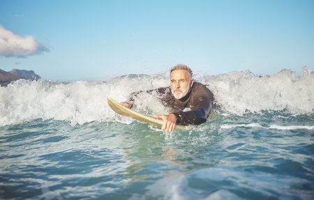 Ocean waves, senior man surfing on beach and healthy fitness lifestyle in Australia summer holiday. Elderly surfer swimming with surfboard, sea water exercise and relax in retirement travel vacationの写真素材