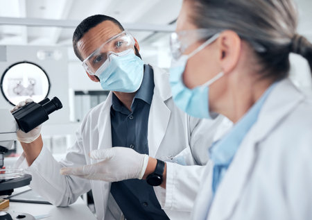 Scientist team, microscope and covid analysis in a research or science lab to study virus for safety, medicine or medical cure. Man and woman biologist collaboration for innovation and breakthroughの写真素材