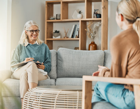 Woman talking with therapist about depression, anxiety and mental health problems in her life. Psychologist listening with patience, understanding and compassion on couch while writing therapy notesの写真素材