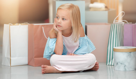 Child, fashion and shopping bags while looking bored and waiting in a kids clothing shop, store or boutique with cute girl sitting on floor. Little kid shopper or customer with sale purchase packagesの写真素材
