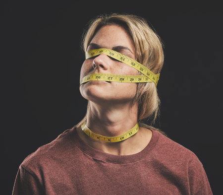 Face, tape measure and stress with an anorexia woman in studio on a dark background for mental...
