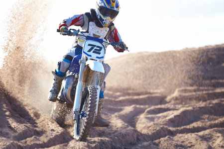 Escaping a sea of sand. A motocross rider riding towards the camera with dirt flying up behind him.の写真素材