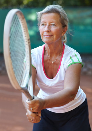 Tennis keeps her healthy. Senior woman preparing to return a serve during a game of tennis.の写真素材