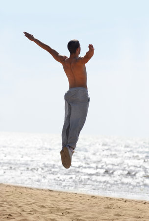 Embracing the day. An athletic young man jumping into the air at the beach.の写真素材