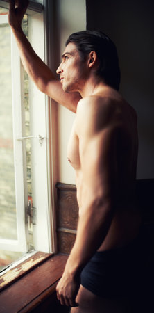 Enjoying the view. Profile of a handsome young shirtless man gazing through the window.の写真素材