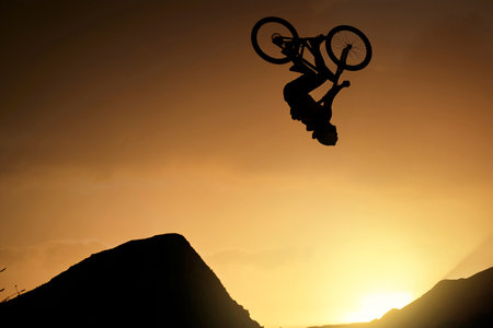 Cyclist, fitness and stunt jump at sunset in Colorado countryside nature mountains in fitness, exercise or training. Danger risk, extreme sports mountain bike or freedom man in sunrise energy workoutの写真素材