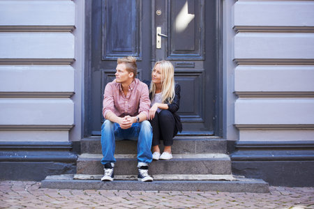 Waiting on some friends. A cute young couple sitting on their doorstep and looking out the street.