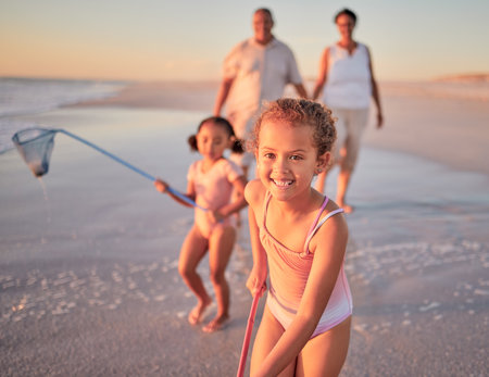 Children, fishing and family with a girl at the beach with her grandparents and sister for summer holiday. Kids, happy and ocean with a child on sand by the sea with her grandmother and grandfatherの写真素材