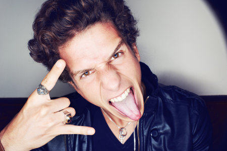 Rock n Roll. Close up portrait of a young man sticking his tongue out and making hand gestures...