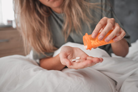 Healthcare, pills in hand and woman in bedroom at home taking prescription medicine. Mental health, depression and medication for health care. Covid, flu and drugs, sick in bed with virus symptoms.の写真素材