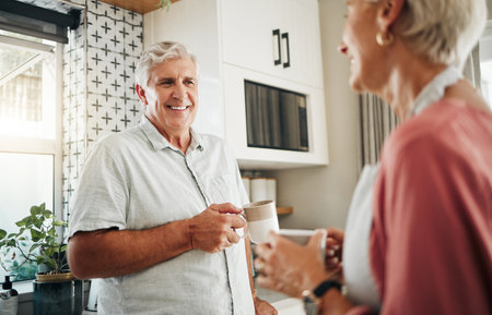 Senior man, drinking coffee and conversation with woman in kitchen at home in New Zealand. Happy, elderly and smile couple enjoy morning tea, chat and relax together in apartment for retirement breakの写真素材