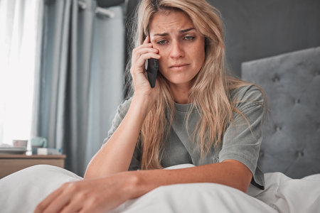 Sad, stress and woman with depression in a phone call conversation in her bedroom worried about a break up. Mental health, anxiety and depressed girl disappointed after listening to bad news at homeの写真素材