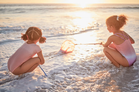 Children, girls and fishing with nets at the beach in playful fun on summer vacation in the...