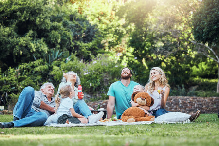 Happy, nature and big family on an outdoor picnic together in a green garden blowing bubbles. Happiness, elderly grandparents and parents relaxing, bonding and playing with children in a outside parkの写真素材